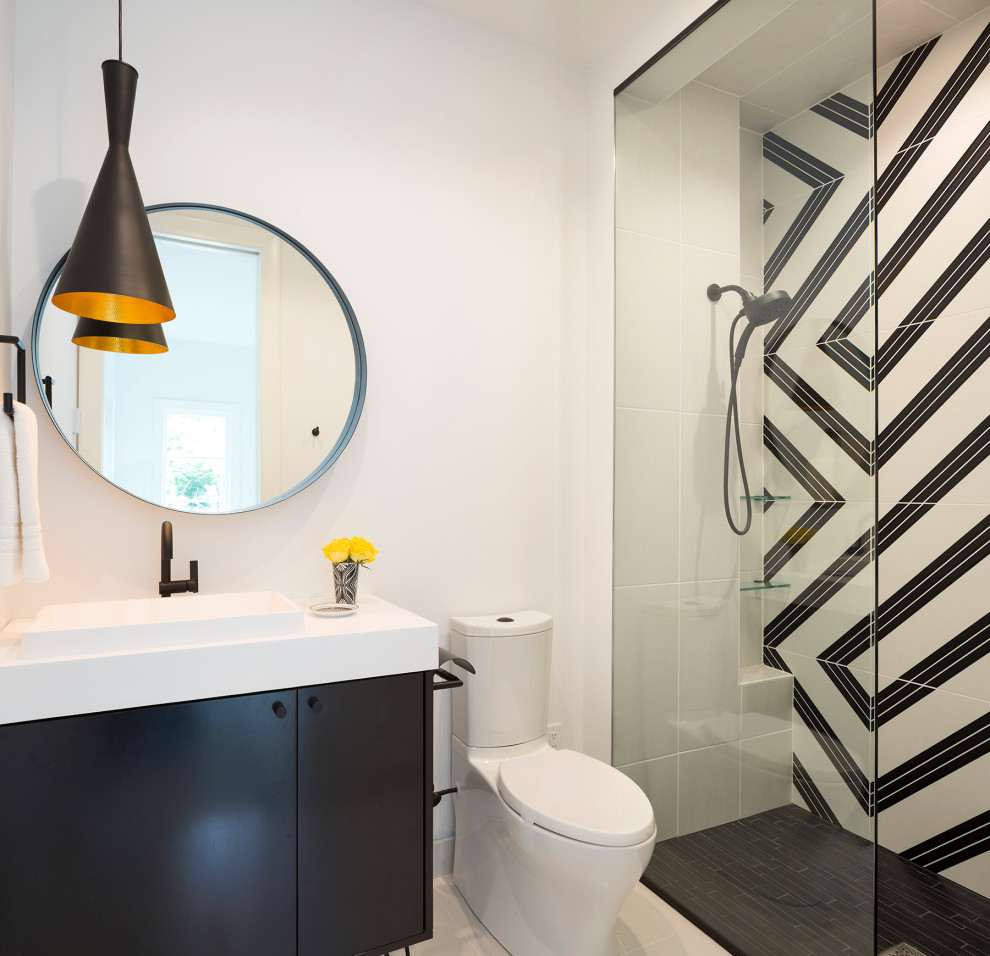 Bild på ett funkis vit vitt badrum med dusch, med släta luckor, svarta skåp, en kantlös dusch, en toalettstol med separat cisternkåpa, svart och vit kakel, vita väggar och ett fristående handfat