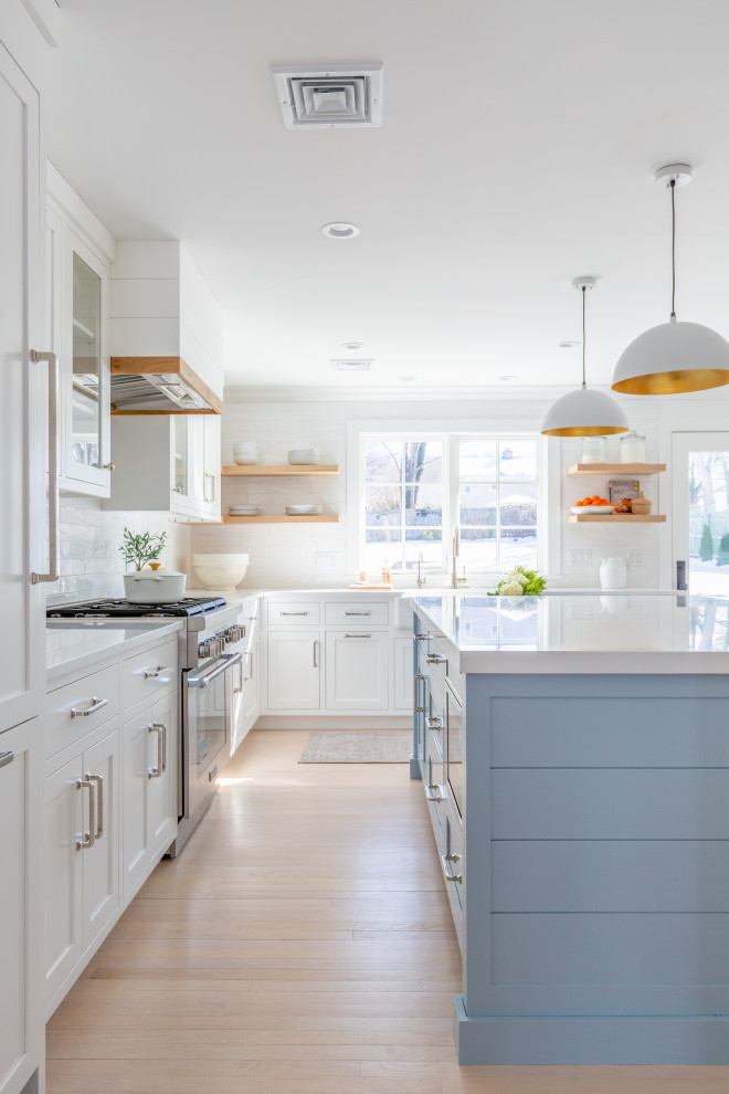 Design ideas for a large beach style l-shaped eat-in kitchen in Other with a farmhouse sink, shaker cabinets, white cabinets, quartz benchtops, white splashback, subway tile splashback, stainless steel appliances, light hardwood floors, with island, beige floor and white benchtop.