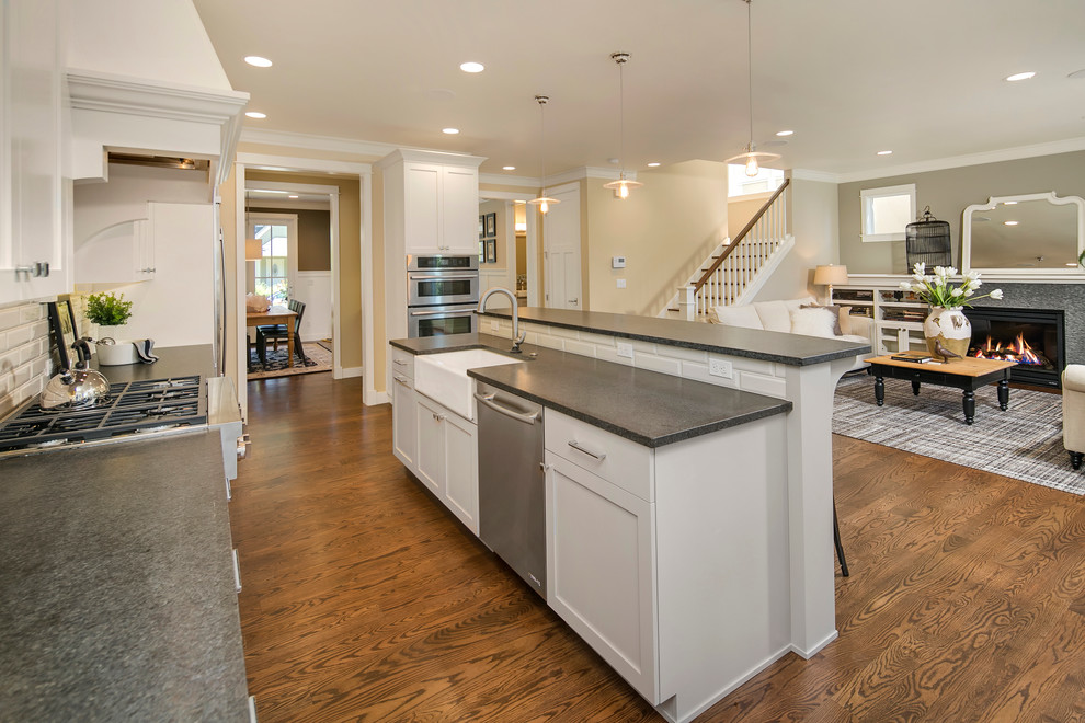 Elegant galley medium tone wood floor eat-in kitchen photo in Seattle with a farmhouse sink, shaker cabinets, white cabinets, granite countertops, gray backsplash, subway tile backsplash, stainless steel appliances and an island