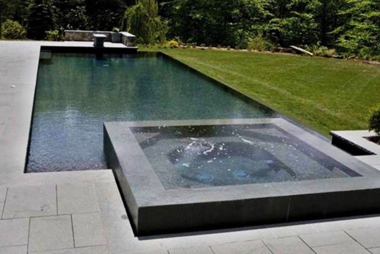 Large modern backyard custom-shaped infinity pool in New York with a hot tub and stamped concrete.