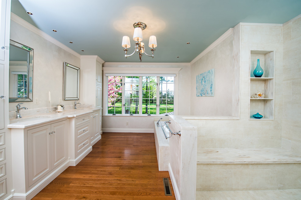 Photo of a mid-sized traditional master bathroom in Philadelphia with an integrated sink, raised-panel cabinets, white cabinets, a drop-in tub, an open shower, a one-piece toilet, beige tile, porcelain tile, white walls and medium hardwood floors.