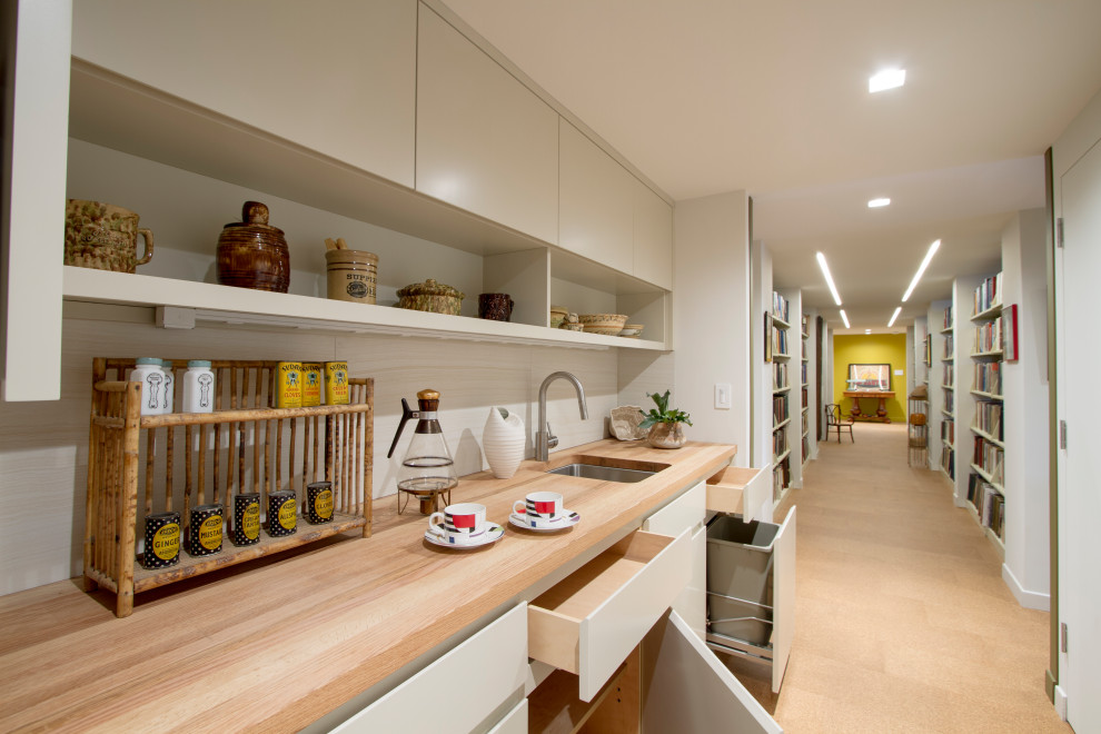 Photo of a small midcentury galley kitchen pantry in New York with a submerged sink, flat-panel cabinets, beige cabinets, wood worktops, white splashback, porcelain splashback, stainless steel appliances, cork flooring, brown floors and brown worktops.