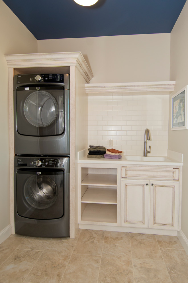 This is an example of a mid-sized traditional single-wall dedicated laundry room in Other with an integrated sink, white cabinets, solid surface benchtops, beige walls, porcelain floors, a stacked washer and dryer and recessed-panel cabinets.
