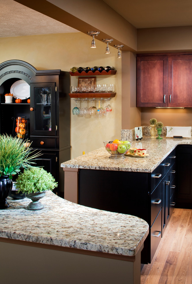 Open concept kitchen - mid-sized transitional u-shaped medium tone wood floor open concept kitchen idea in Omaha with shaker cabinets, dark wood cabinets, granite countertops, beige backsplash, stone slab backsplash, stainless steel appliances, a peninsula and an undermount sink