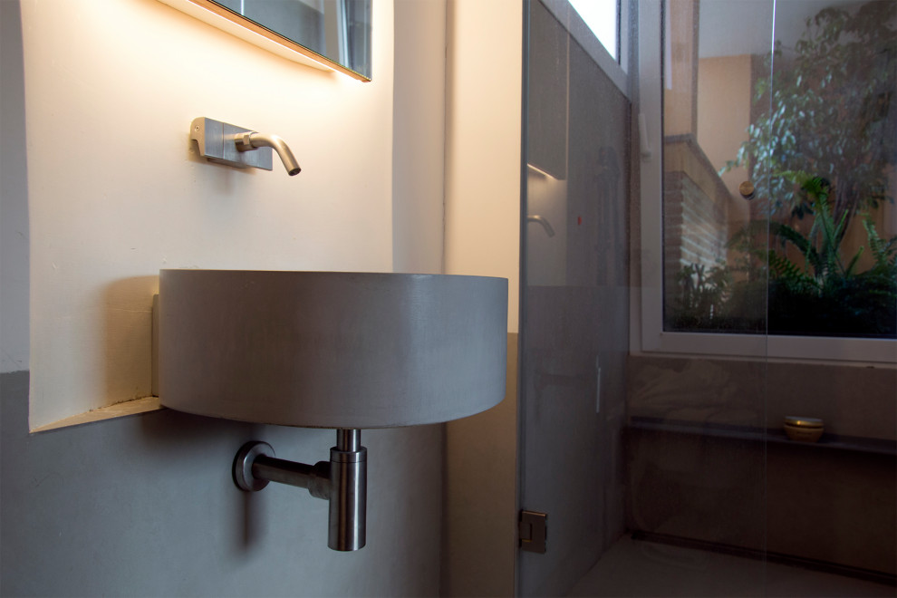 Photo of a small contemporary powder room in Rome with a two-piece toilet, gray tile, porcelain tile, white walls, porcelain floors, a wall-mount sink, concrete benchtops, grey floor, a floating vanity, recessed and grey benchtops.