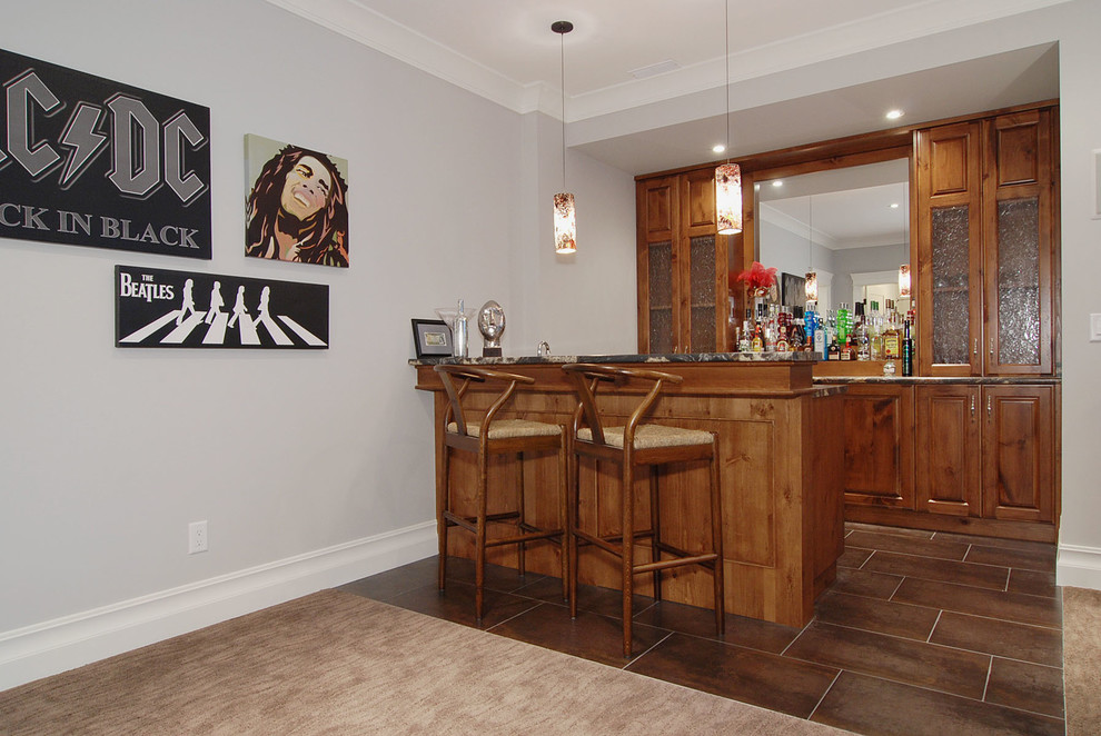This is an example of a mid-sized arts and crafts seated home bar in Vancouver with porcelain floors, an undermount sink, recessed-panel cabinets, medium wood cabinets, granite benchtops and mirror splashback.