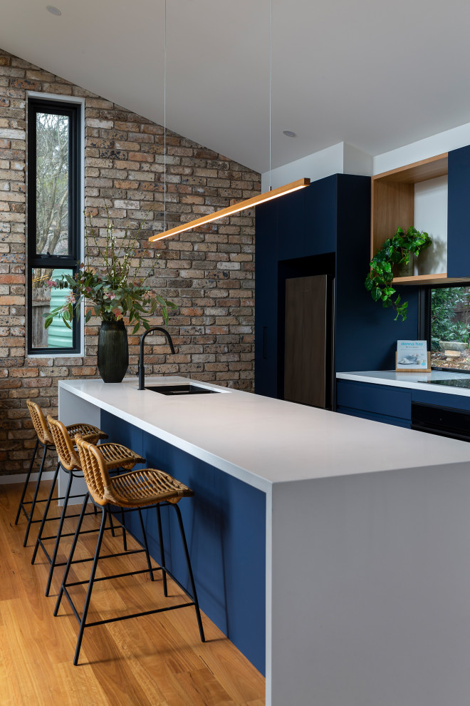 Medium sized contemporary galley open plan kitchen in Canberra - Queanbeyan with a submerged sink, all styles of cabinet, blue cabinets, engineered stone countertops, window splashback, black appliances, medium hardwood flooring, an island and white worktops.