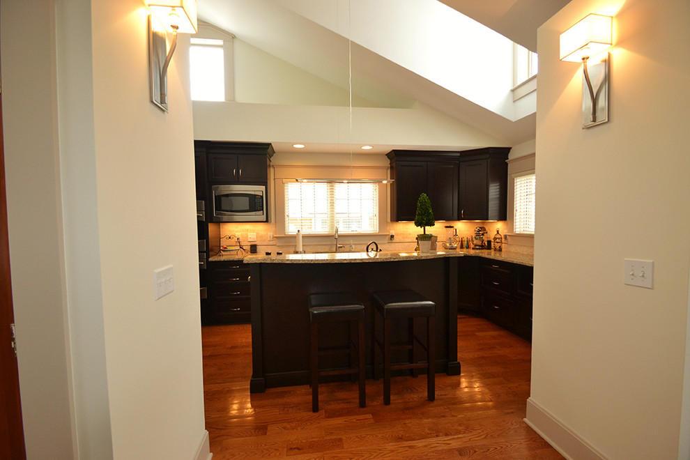 Large transitional galley medium tone wood floor home design photo in Columbus with an undermount sink, recessed-panel cabinets, dark wood cabinets, granite countertops, beige backsplash, stone tile backsplash, stainless steel appliances and an island