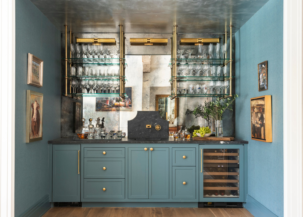 This is an example of a transitional single-wall wet bar in Houston with light hardwood floors, shaker cabinets, blue cabinets, mirror splashback and black benchtop.