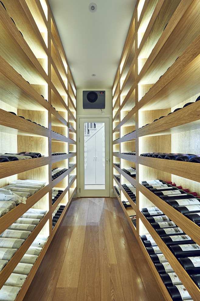 Mid-sized contemporary wine cellar in London with light hardwood floors and storage racks.