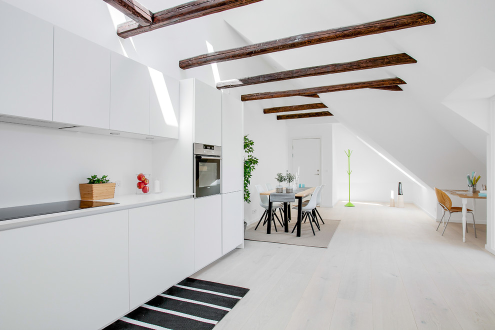 This is an example of a mid-sized scandinavian single-wall open plan kitchen in Copenhagen with flat-panel cabinets, white cabinets, stainless steel appliances, light hardwood floors, laminate benchtops and no island.