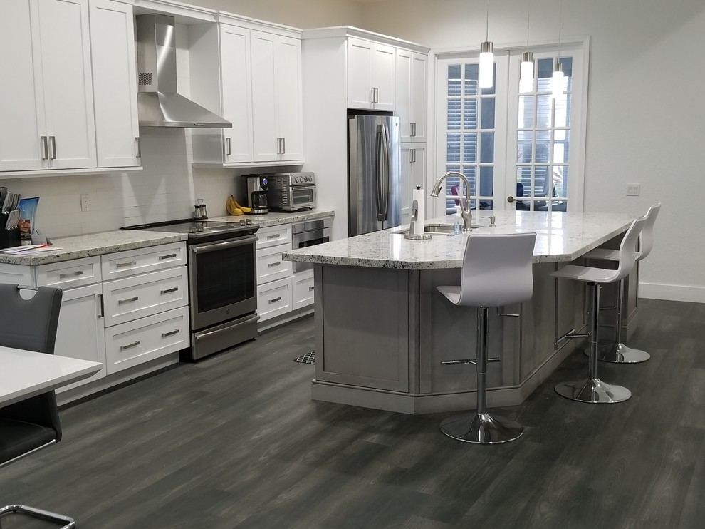 Photo of a mid-sized transitional single-wall eat-in kitchen in Miami with an undermount sink, shaker cabinets, white cabinets, granite benchtops, white splashback, subway tile splashback, stainless steel appliances, porcelain floors, with island, black floor and white benchtop.