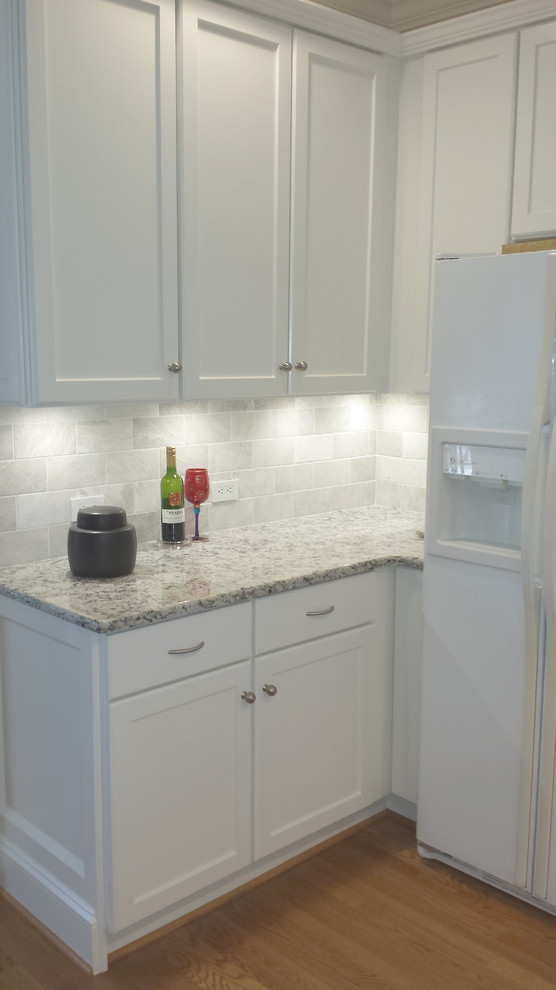 Mid-sized transitional l-shaped light wood floor eat-in kitchen photo with an undermount sink, recessed-panel cabinets, white cabinets, granite countertops, white backsplash, stone tile backsplash, white appliances and a peninsula