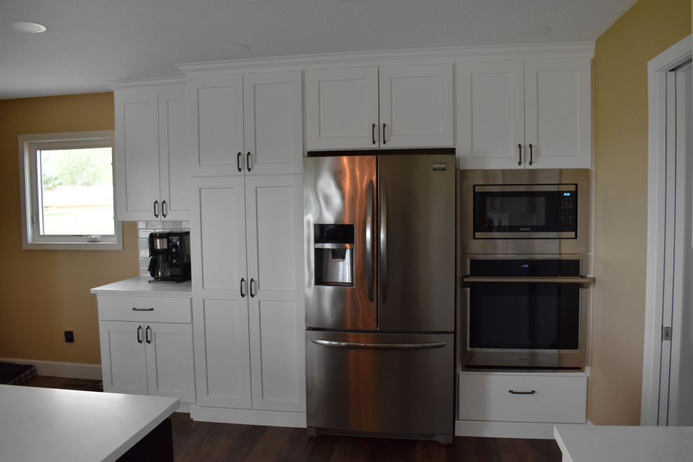 Open concept kitchen - large modern l-shaped vinyl floor and brown floor open concept kitchen idea with a drop-in sink, yellow cabinets, quartzite countertops, yellow backsplash, subway tile backsplash, stainless steel appliances, an island and white countertops