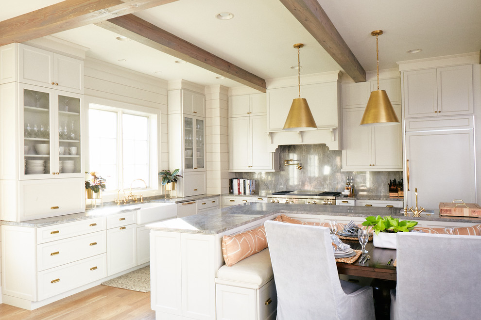 Large transitional l-shaped medium tone wood floor and brown floor eat-in kitchen photo with a farmhouse sink, raised-panel cabinets, white cabinets, marble countertops, gray backsplash, marble backsplash, stainless steel appliances, an island and gray countertops