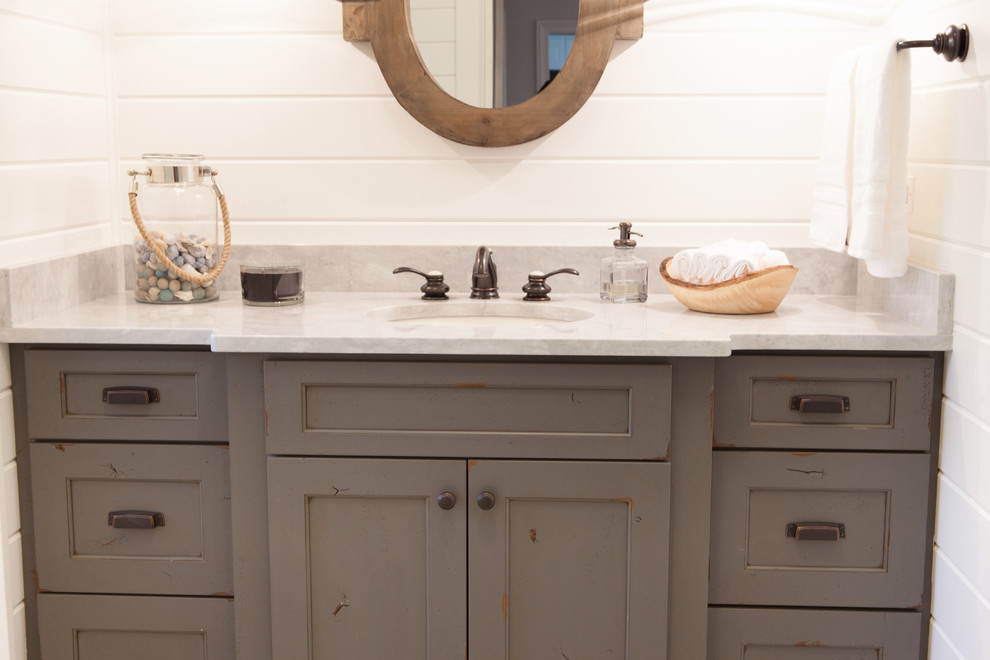 Photo of a small country powder room in Chicago with an undermount sink, distressed cabinets, marble benchtops, a two-piece toilet, white walls, beaded inset cabinets, gray tile and white tile.