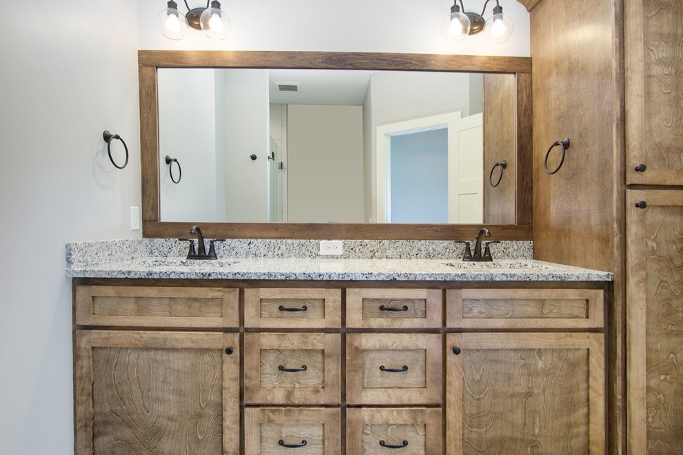 This is an example of a mid-sized country 3/4 bathroom in Grand Rapids with shaker cabinets, medium wood cabinets, an alcove shower, a two-piece toilet, white tile, porcelain tile, grey walls, slate floors, an undermount sink, granite benchtops, grey floor, a hinged shower door and grey benchtops.