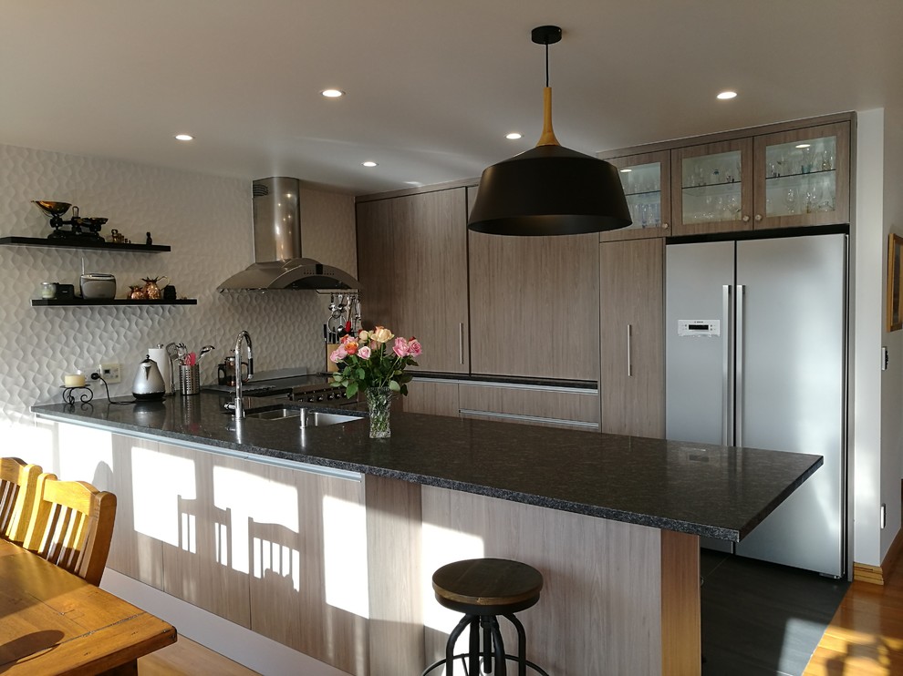 Inspiration for a mid-sized contemporary u-shaped eat-in kitchen in Wellington with a double-bowl sink, flat-panel cabinets, medium wood cabinets, granite benchtops, white splashback, porcelain splashback, stainless steel appliances, medium hardwood floors, with island, brown floor and grey benchtop.