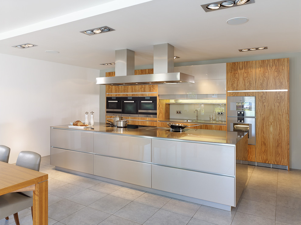 This is an example of a large contemporary single-wall open plan kitchen in Dusseldorf with a single-bowl sink, flat-panel cabinets, medium wood cabinets, white splashback, glass sheet splashback, stainless steel appliances, with island, quartz benchtops and beige benchtop.