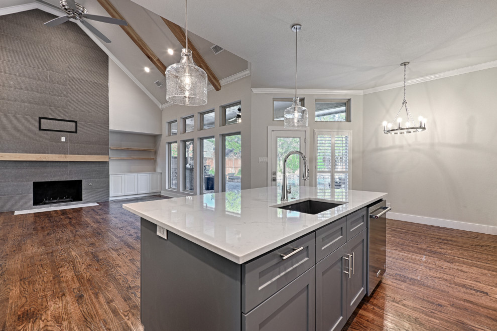 This is an example of a traditional l-shaped kitchen in Dallas with a submerged sink, shaker cabinets, white cabinets, engineered stone countertops, grey splashback, porcelain splashback, stainless steel appliances, medium hardwood flooring, an island, brown floors and white worktops.
