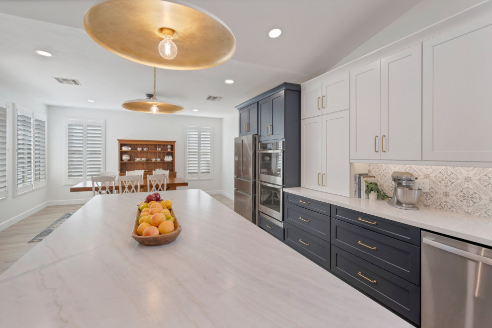 Example of a large transitional l-shaped porcelain tile, brown floor and vaulted ceiling eat-in kitchen design in Phoenix with an undermount sink, shaker cabinets, blue cabinets, quartzite countertops, multicolored backsplash, mosaic tile backsplash, stainless steel appliances, two islands and white countertops