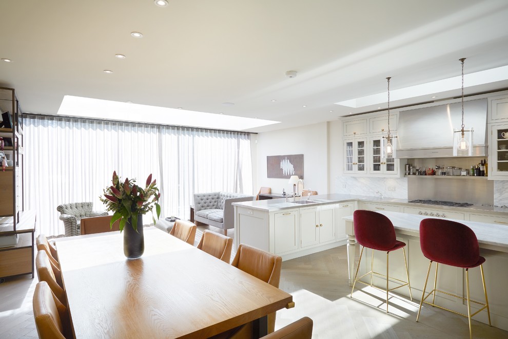 Large contemporary u-shaped open plan kitchen in London with white cabinets, marble benchtops, metallic splashback, stainless steel appliances, light hardwood floors, a peninsula and beige floor.