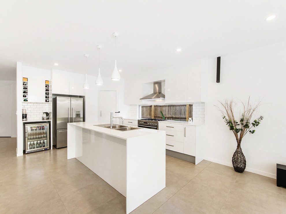 This is an example of a beach style kitchen in Gold Coast - Tweed with a double-bowl sink, flat-panel cabinets, white cabinets, window splashback, stainless steel appliances, concrete floors, with island, beige floor and white benchtop.
