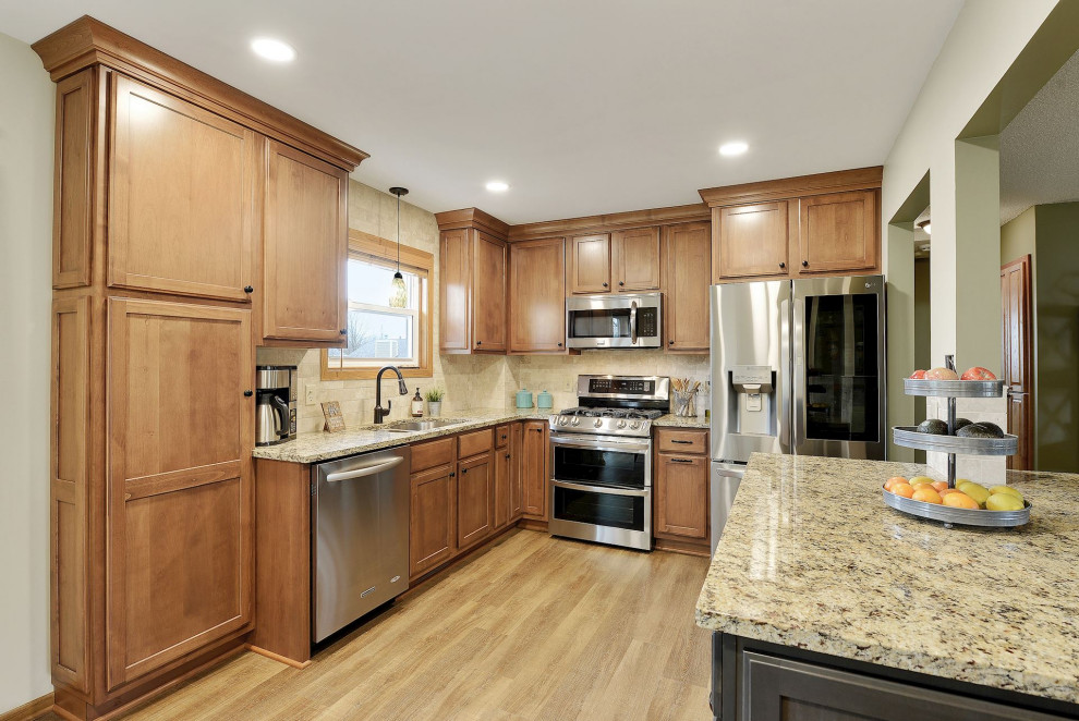 Inspiration for a small transitional u-shaped vinyl floor and brown floor open concept kitchen remodel in Minneapolis with an undermount sink, shaker cabinets, medium tone wood cabinets, granite countertops, beige backsplash, travertine backsplash, stainless steel appliances, an island and multicolored countertops