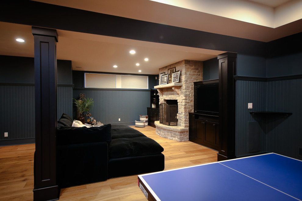 Large traditional fully buried basement in Other with a home bar, blue walls, light hardwood flooring, a standard fireplace and a stone fireplace surround.