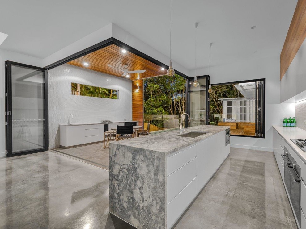 Design ideas for a large modern galley open plan kitchen in Brisbane with an undermount sink, white cabinets, marble benchtops, grey splashback, glass tile splashback, stainless steel appliances, concrete floors, with island, grey floor and grey benchtop.