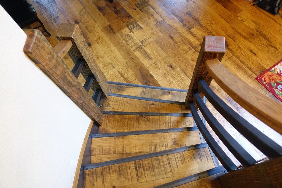 На фото: большая изогнутая лестница в стиле рустика с деревянными ступенями, подступенками из сланца и деревянными перилами