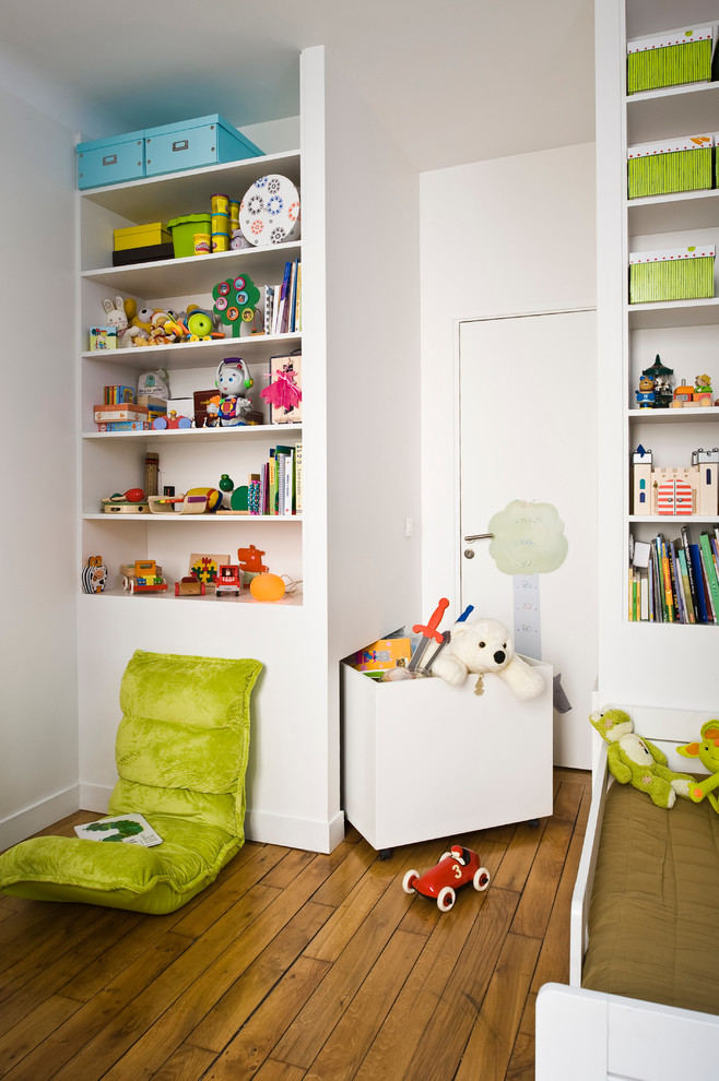 This is an example of a small contemporary gender-neutral kids' room for kids 4-10 years old in Paris with white walls, medium hardwood floors and brown floor.