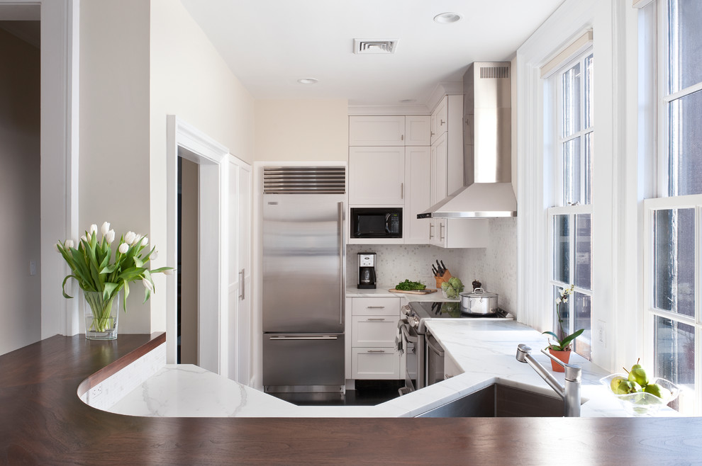 Photo of a transitional u-shaped kitchen in Boston with marble benchtops, an undermount sink, recessed-panel cabinets, white cabinets, white splashback, mosaic tile splashback and stainless steel appliances.