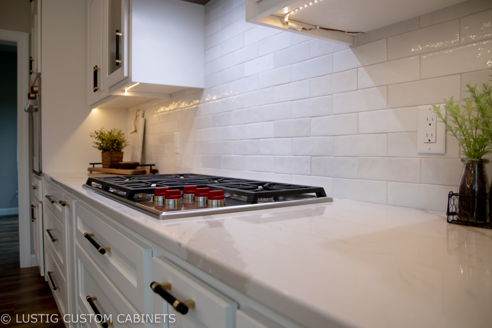 Inspiration for a large transitional l-shaped laminate floor and brown floor open concept kitchen remodel with an undermount sink, flat-panel cabinets, white cabinets, quartz countertops, white backsplash, ceramic backsplash, stainless steel appliances, an island and white countertops