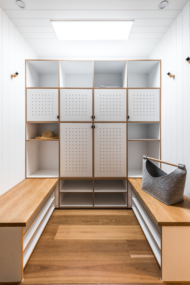 Photo of a contemporary gender-neutral dressing room in Melbourne with flat-panel cabinets, white cabinets, medium hardwood floors and brown floor.