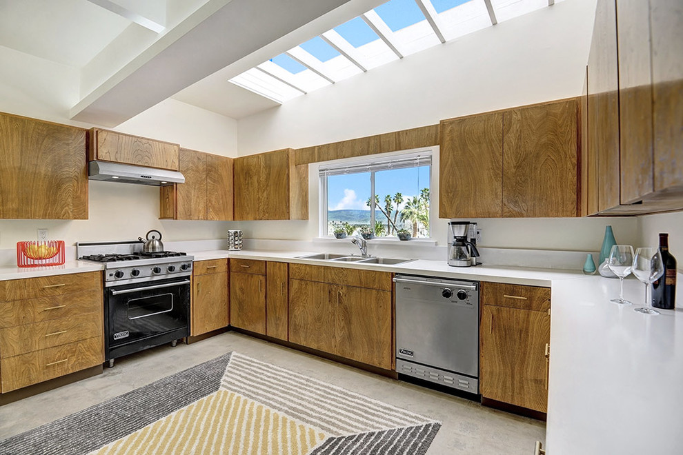 Photo of a midcentury u-shaped separate kitchen in Los Angeles with a double-bowl sink, flat-panel cabinets, medium wood cabinets, white splashback, black appliances, no island and grey floor.