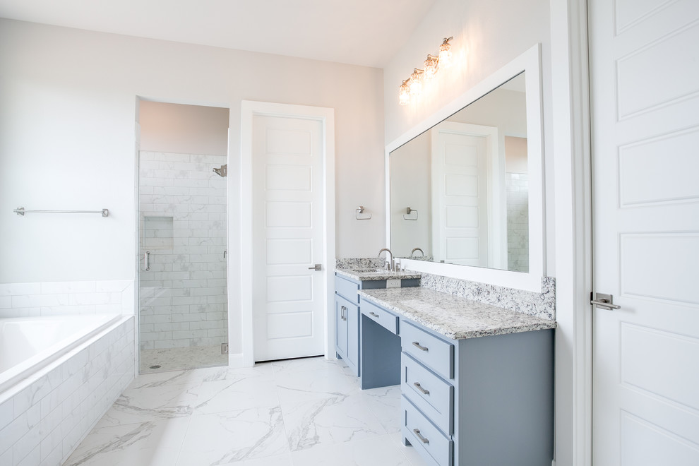 This is an example of a large transitional master bathroom in Dallas with shaker cabinets, blue cabinets, a curbless shower, a one-piece toilet, white tile, marble, white walls, ceramic floors, an undermount sink, granite benchtops, white floor and a hinged shower door.