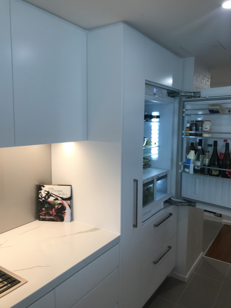 Mid-sized contemporary galley kitchen in Newcastle - Maitland with an undermount sink, flat-panel cabinets, white cabinets, quartz benchtops, white splashback, glass sheet splashback, stainless steel appliances, with island, porcelain floors and grey floor.