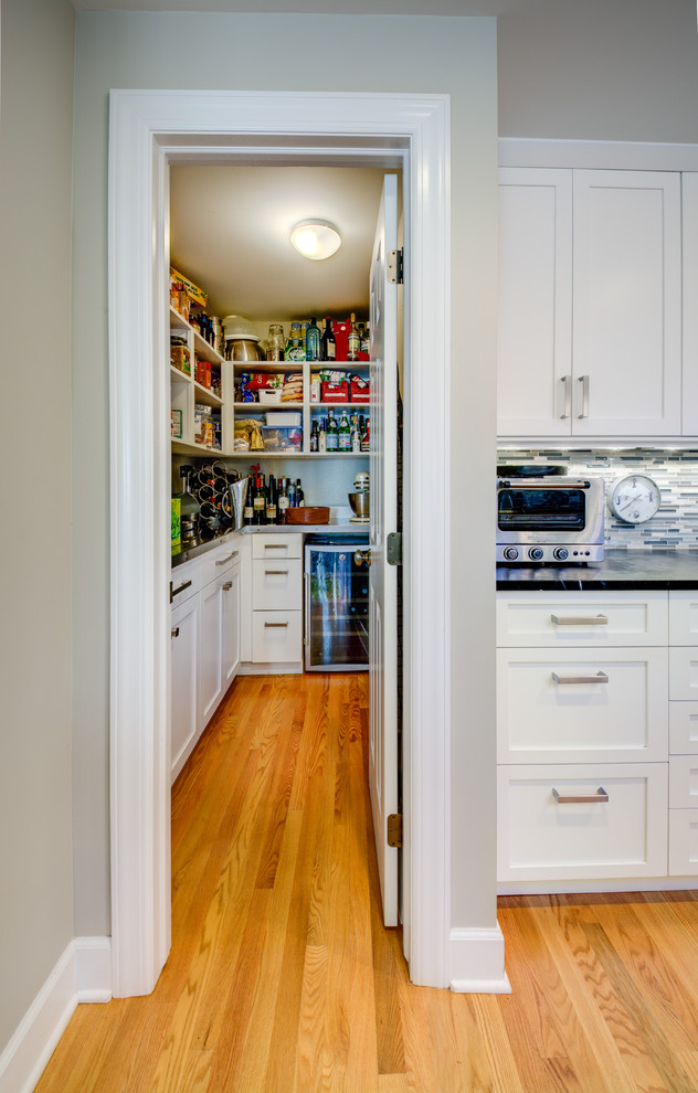 Mid-sized elegant l-shaped medium tone wood floor kitchen pantry photo in Detroit with recessed-panel cabinets, white cabinets and stainless steel countertops