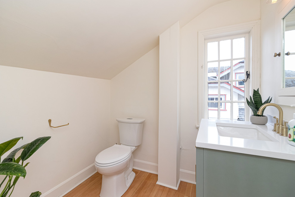Toilet room - small transitional medium tone wood floor, white floor, single-sink and vaulted ceiling toilet room idea with flat-panel cabinets, turquoise cabinets, a two-piece toilet, white walls, a drop-in sink, soapstone countertops, white countertops and a freestanding vanity