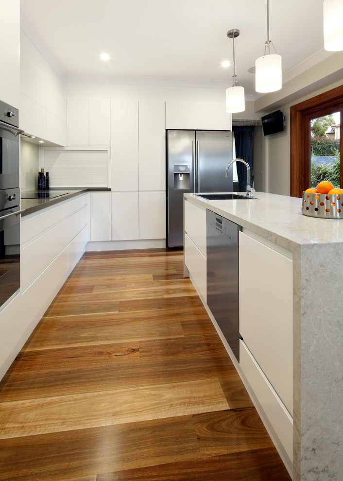 Inspiration for a mid-sized modern l-shaped kitchen in Sydney with a single-bowl sink, flat-panel cabinets, white cabinets, quartz benchtops, white splashback, glass sheet splashback, medium hardwood floors and with island.