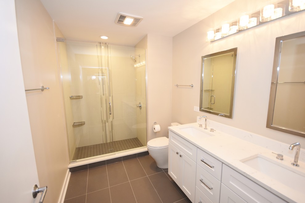 Inspiration for a mid-sized contemporary wet room bathroom in Chicago with shaker cabinets, white cabinets, a one-piece toilet, beige tile, ceramic tile, beige walls, ceramic floors, a drop-in sink, engineered quartz benchtops, brown floor, a hinged shower door and white benchtops.