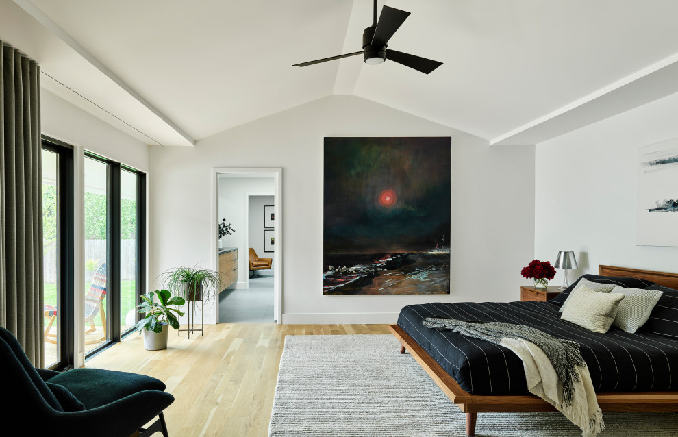 Réalisation d'une grande chambre parentale minimaliste avec un mur blanc, parquet clair et un plafond voûté.