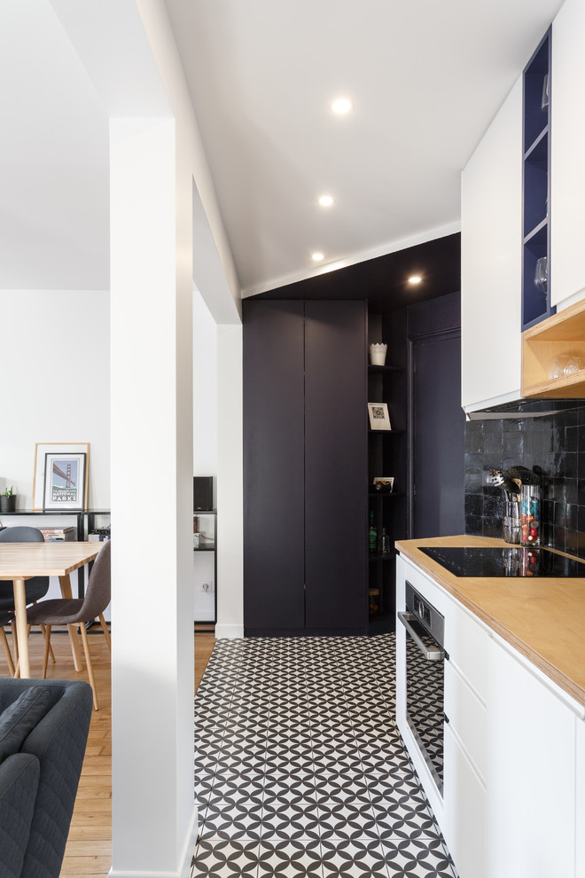 Photo of a small modern single-wall open plan kitchen in Paris with a drop-in sink, flat-panel cabinets, white cabinets, wood benchtops, black splashback, terra-cotta splashback, stainless steel appliances, cement tiles, no island, multi-coloured floor and beige benchtop.