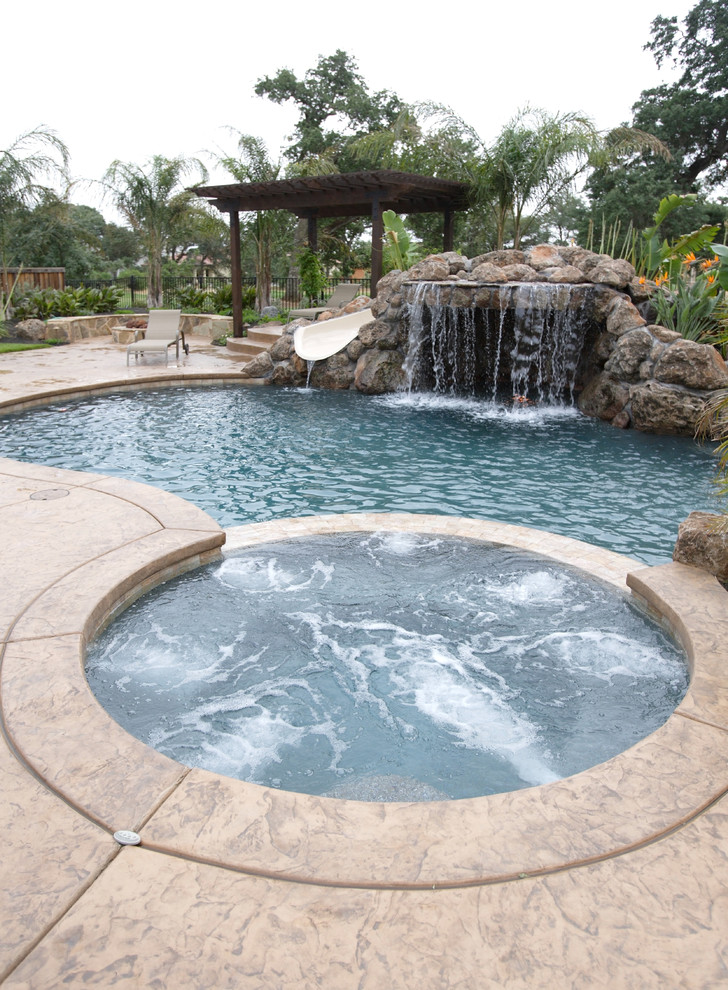 Photo of a mid-sized tropical backyard custom-shaped natural pool in San Diego with a water slide and stamped concrete.