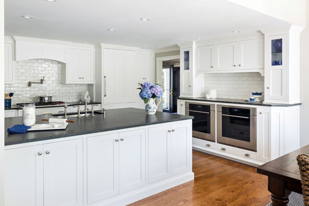 Inspiration for a large beach style l-shaped open plan kitchen in Boston with an undermount sink, recessed-panel cabinets, white cabinets, granite benchtops, white splashback, ceramic splashback, stainless steel appliances, medium hardwood floors and with island.