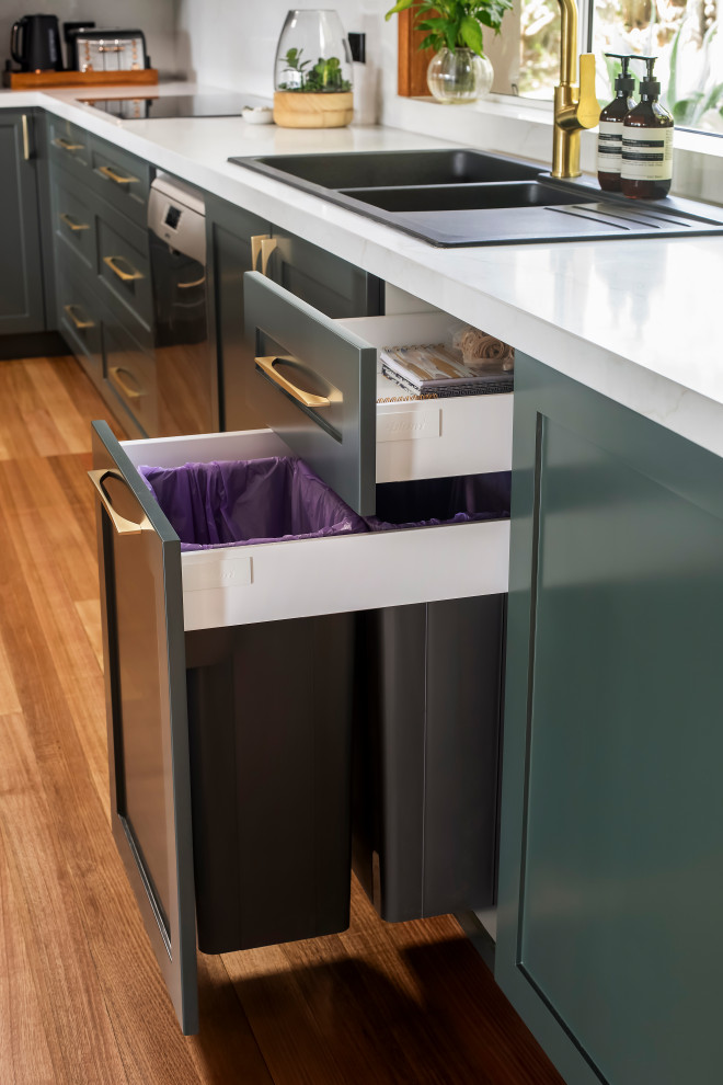 Example of a large transitional l-shaped medium tone wood floor and multicolored floor eat-in kitchen design in Sydney with a drop-in sink, shaker cabinets, green cabinets, quartz countertops, white backsplash, quartz backsplash, black appliances, an island and white countertops