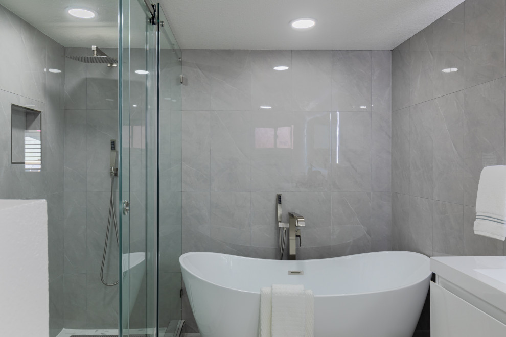 Photo of a mid-sized contemporary master bathroom in San Diego with white cabinets, a corner shower, gray tile, ceramic tile, white walls, ceramic floors, an integrated sink, engineered quartz benchtops, a sliding shower screen, white benchtops, flat-panel cabinets, a floating vanity, a corner tub, a one-piece toilet, grey floor, a double vanity and brick walls.
