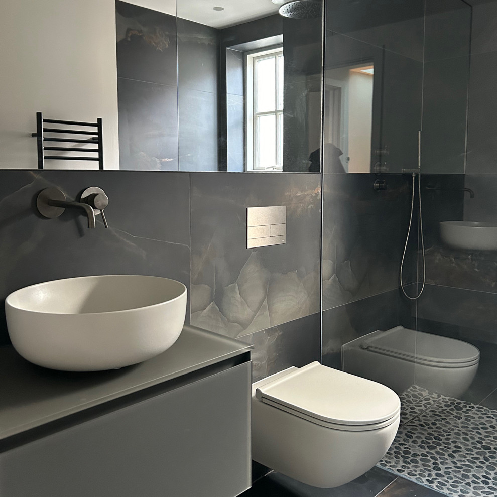 Inspiration for a small modern 3/4 bathroom in London with flat-panel cabinets, grey cabinets, an open shower, a wall-mount toilet, black tile, ceramic tile, pebble tile floors, a console sink, glass benchtops, black floor, an open shower, a single vanity and a floating vanity.