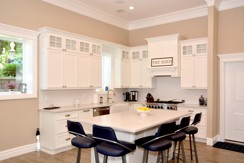 Example of a mid-sized transitional l-shaped beige floor and porcelain tile open concept kitchen design in New York with a farmhouse sink, shaker cabinets, white cabinets, granite countertops, white backsplash, subway tile backsplash, stainless steel appliances, an island and white countertops